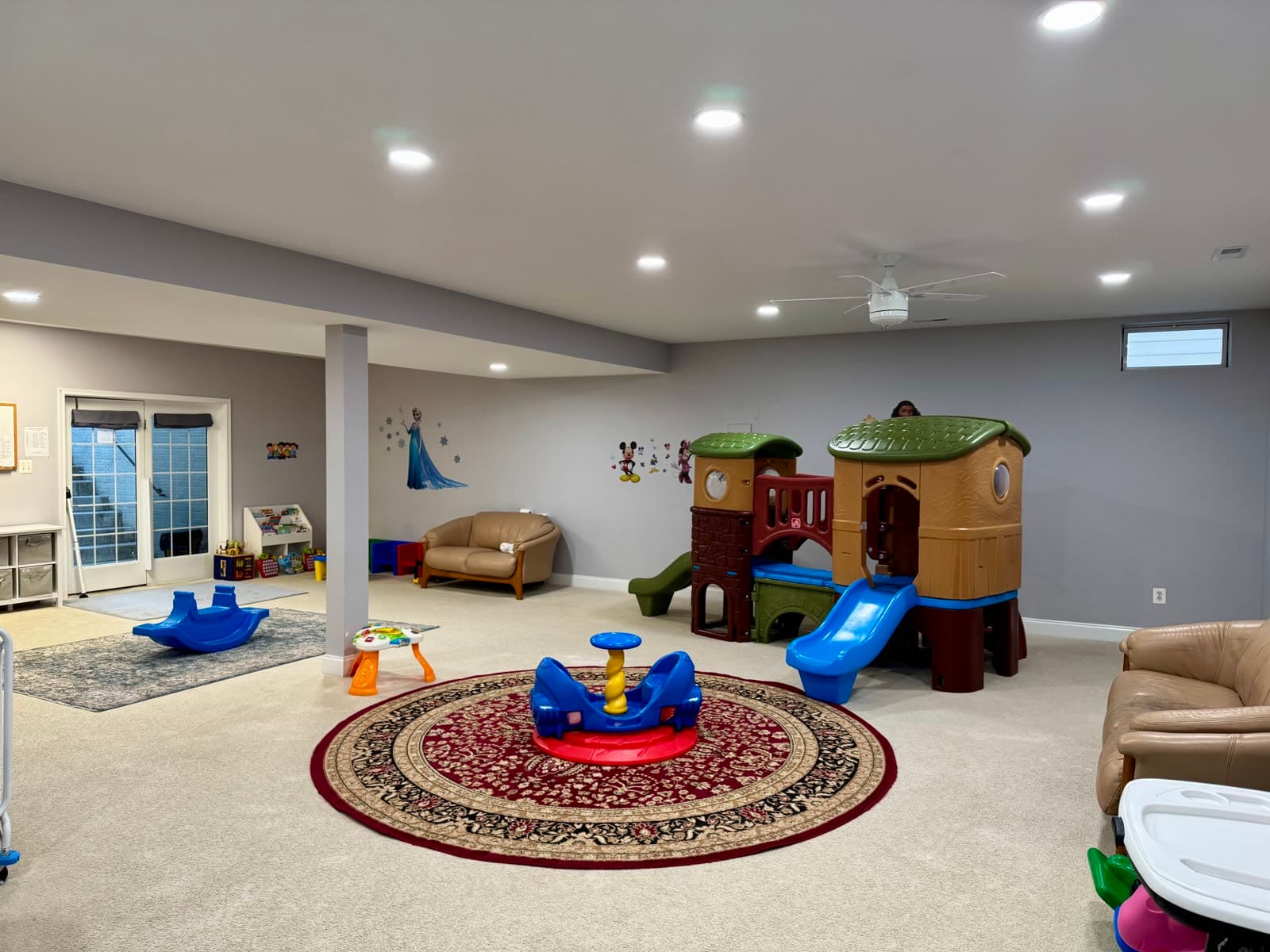 Open playroom with a wooden climbing structure with slides, ride-on toys, and cozy seating.