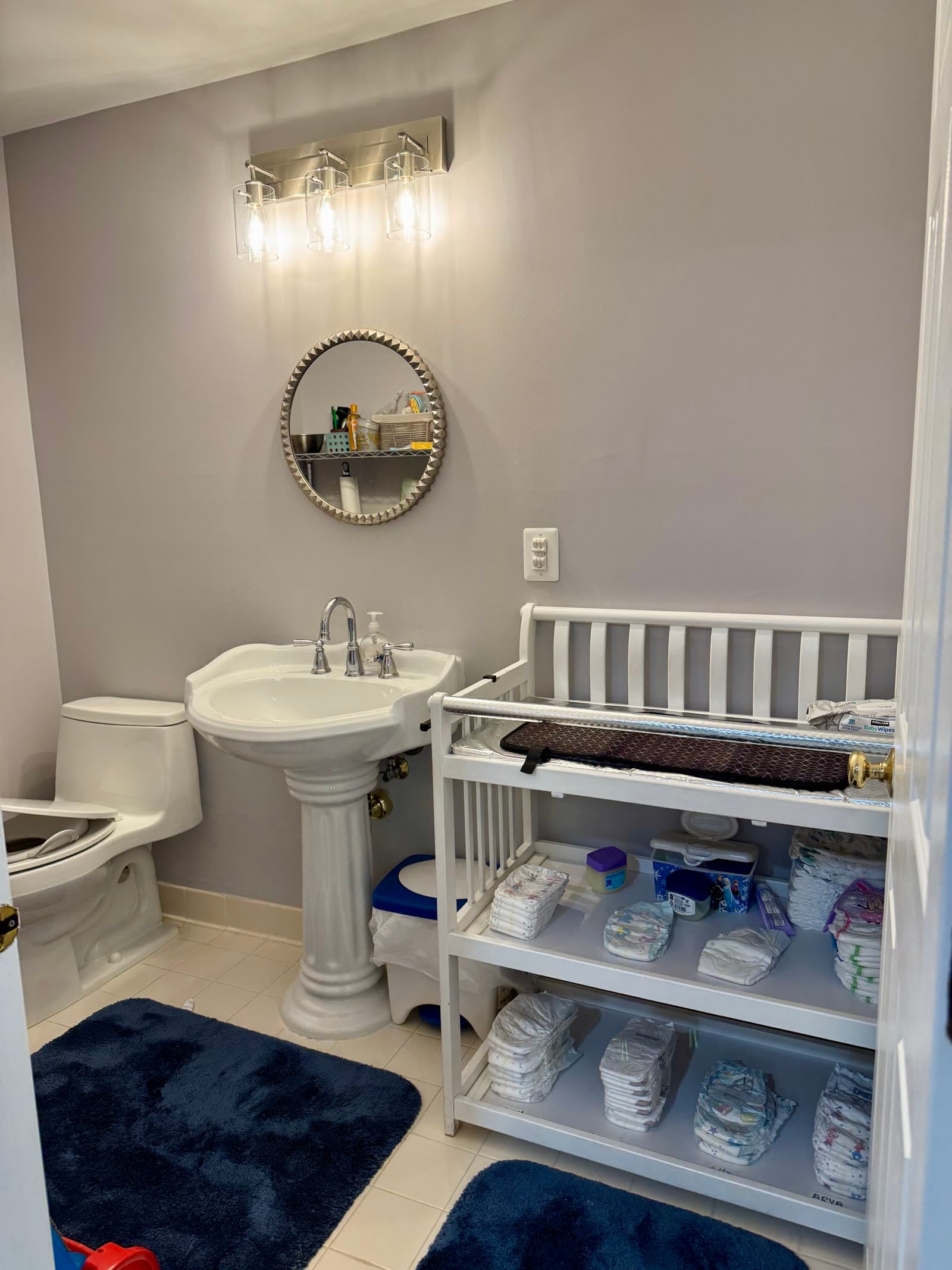 Changing station stocked with diapers and wipes next to the bathroom sink and toilet.