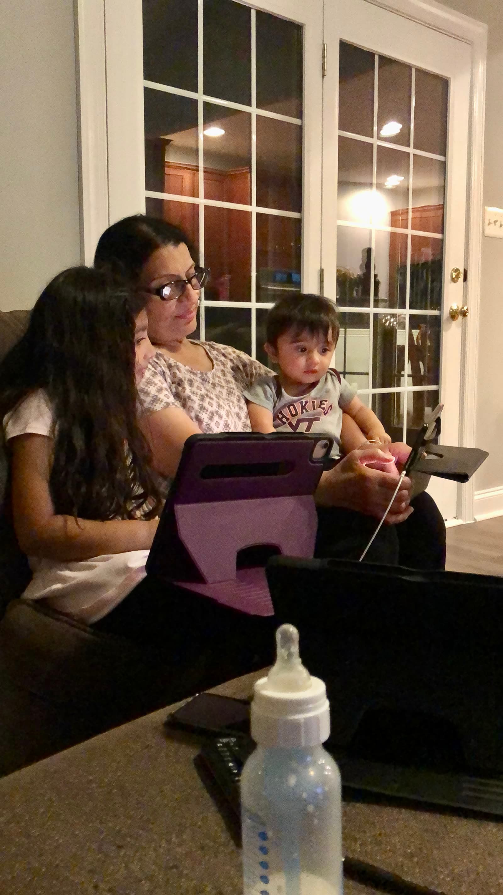 Shahnaz sitting with children on a couch, reading together on a tablet in the evening.